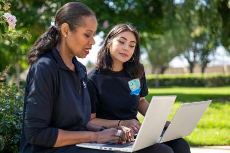 Two people sitting on a bench with laptops, working together.